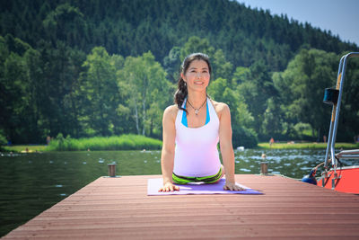 Smiling woman exercising on pier over river