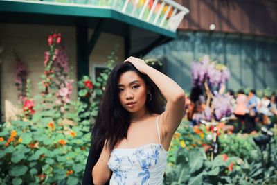 Portrait of beautiful young woman standing by flowering plants