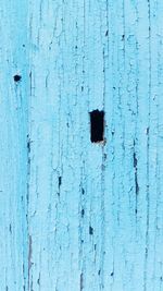 Close-up of hole in blue wooden wall