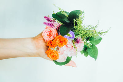 Close-up of hand holding bouquet against white background