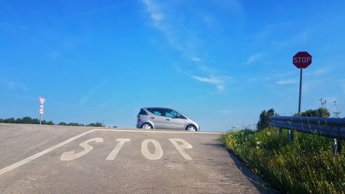 Car by stop sign on road against blue sky