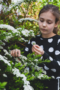 Cute girl holding flowering plant while standing outdoors