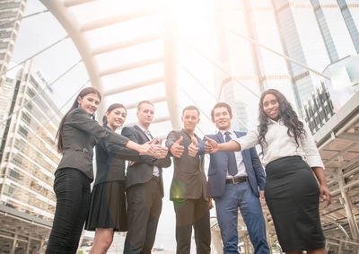 Low angle portrait of confident business colleagues gesturing thumbs up while standing in city