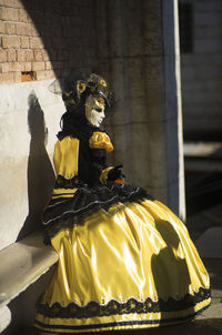 Woman wearing mask and costume sitting on bench during carnival of venice