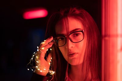Portrait of young woman holding illuminated string lights while standing outdoors at night