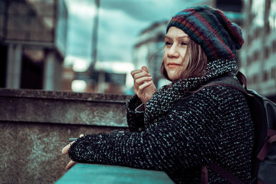 Woman in warm clothing standing by retaining wall in city