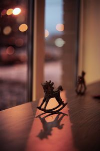 Close-up of rocking horse figurine on table against window at dusk