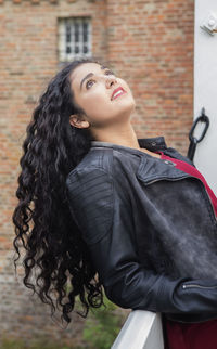 Teenage girl looking up while standing against building 