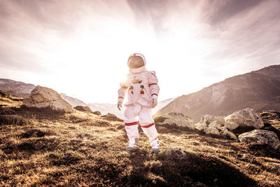 Low angle view of child standing on rock against sky