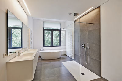 Bathtub in corian, faucet and shower in tiled bathroom with windows towards garden