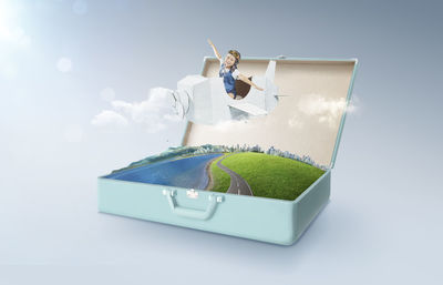 Digital composite image of girl flying in airplane over briefcase against sky