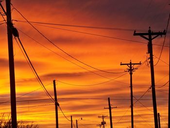 Low angle view of silhouette power lines against sky during sunset