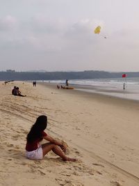 Women relaxing on beach against sky