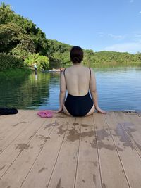 Rear view of woman sitting by lake against sky