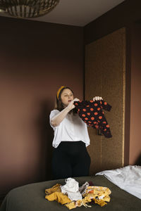 Young woman holding umbrella standing on table against wall