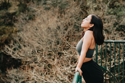 Side view of young woman standing by railing