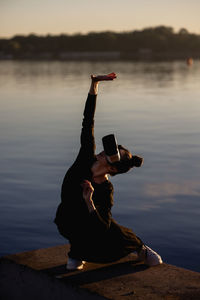 Side view of woman drinking water while standing at beach during sunset