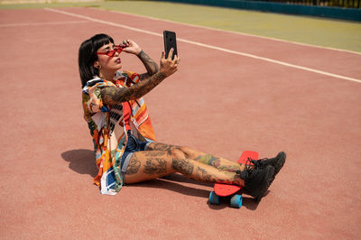 Caucasian girl with tattoos and short black hair on a sports court making a video call