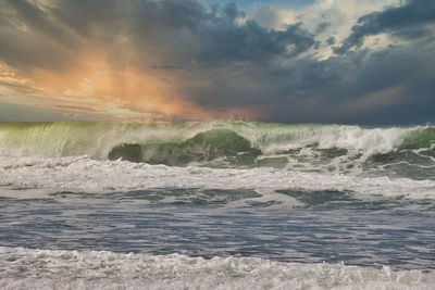 Sea waves splashing on shore against sky during sunset