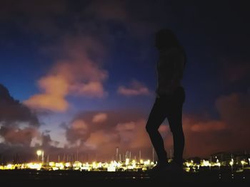 Silhouette man standing by illuminated city against sky at night