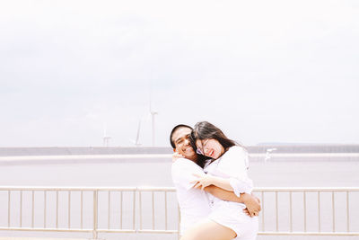 Man lifting woman while standing by railing against sea and sky