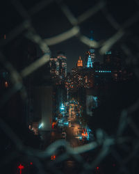 High angle of a street in new york city at night taken through a fence with the manhattan skyline 
