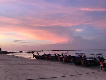 Longtail boats moored at beach against cloudy sky during sunset