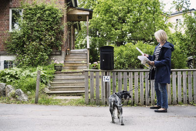 Senior woman checking letters while standing with dog outside house