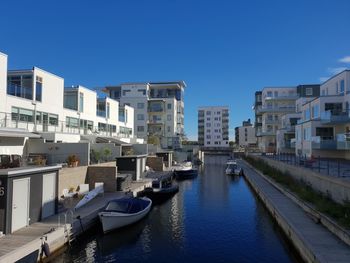 Boats in canal amidst buildings in city against clear blue sky