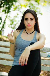 Portrait of young woman showing obscene gesture while sitting on bench
