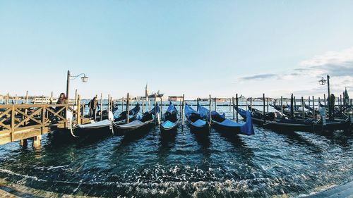 Gondolas moored on canal against blue sky