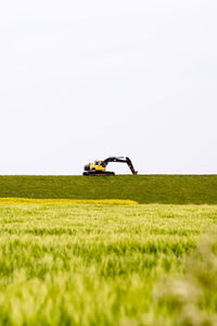 Earth mover on grassy field against clear sky