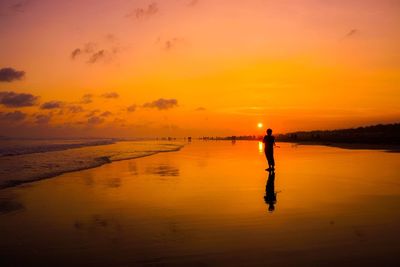 Silhouette man standing on beach against orange sky