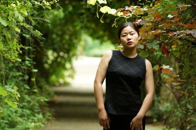 Portrait of young woman standing against trees at park