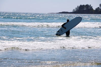 Silhouette man with surfboard standing in sea against clear sky