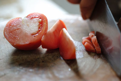 Cropped image of hands chopping tomatoes on wooden cutting board