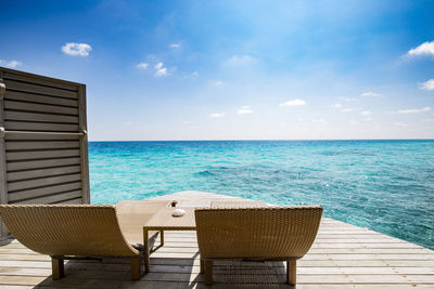 Chairs by swimming pool at beach against sky