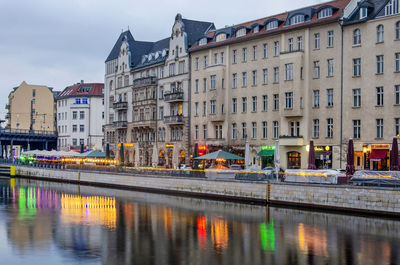 Cafes and restaurants on schiffbauerdam reflect in the river spree at dusk