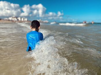 Young boy sitting away from camera in the ocean