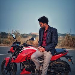 Young man sitting on motorcycle on road against sky