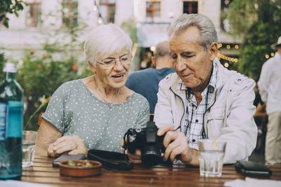 Senior man showing camera to woman while sitting at restaurant in city