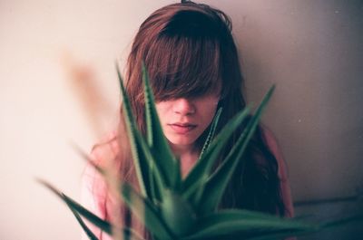 Sad woman standing behind aloe vera against wall at home