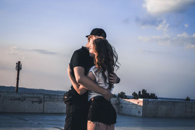 Couple embracing while standing on terrace against sky