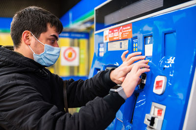 Side view of blind male in medical mask paying for ticket in terminal in metro