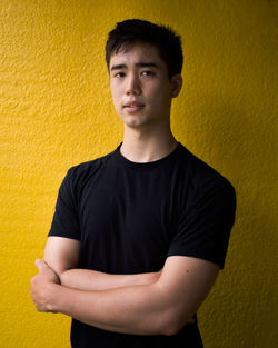 Portrait of young man standing against yellow wall