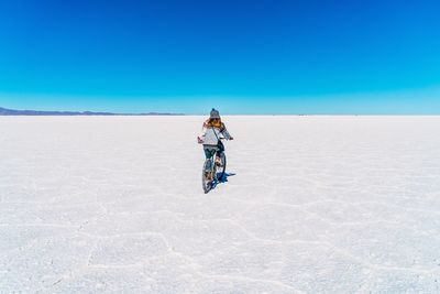 Rear view of mid adult woman riding bicycle on snow covered field