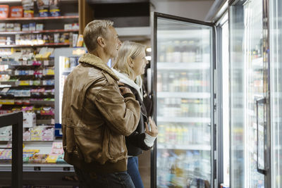 Smiling mature couple doing shopping from refrigerated section at supermarket