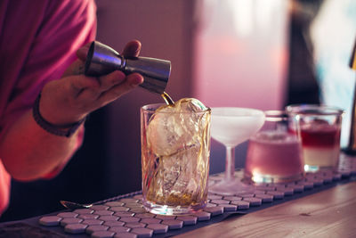 Cropped hand of person pouring alcohol in glass at bar counter