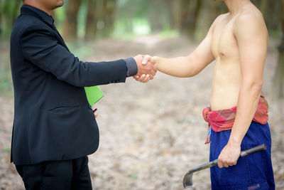 Midsection of manager and shirtless worker handshaking on field