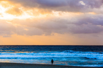 Woman fishing on scenic sea against sky during sunset